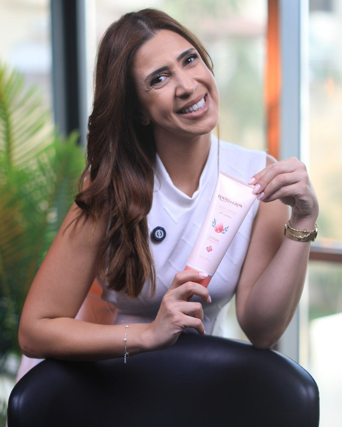 A model seated by a window, holding Julnar Body Lotion.